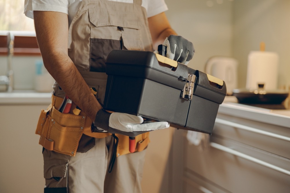 Handyman holding a toolbox in a kitchen setting, illustrating home improvement services and maintenance tasks.